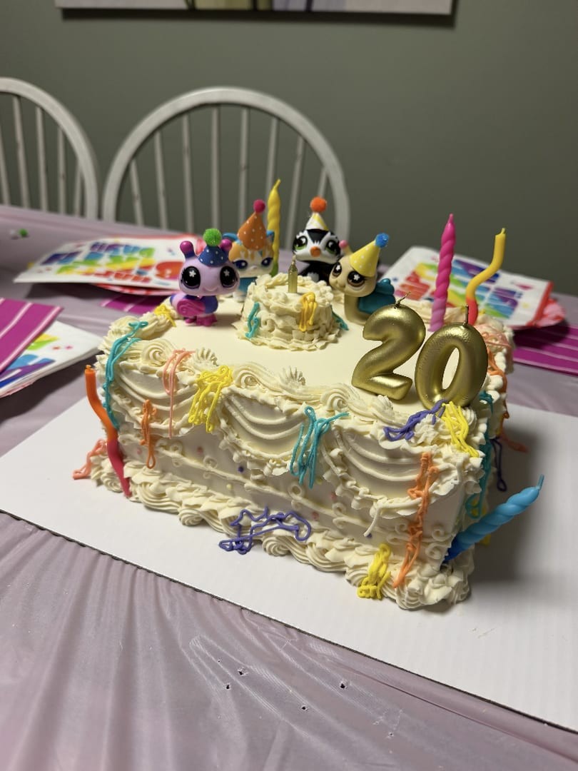 Rectangular birthday cake with white ruffled frosting, rainbow candles, and a gold number 20