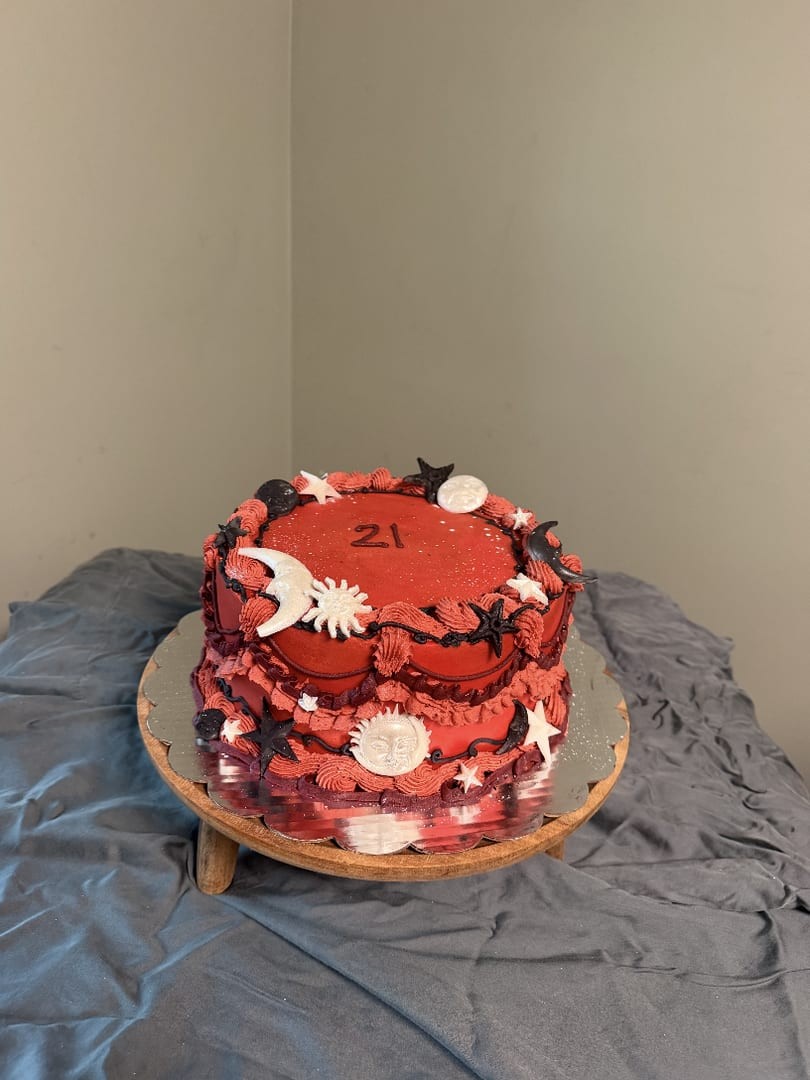 Round red cake with scalloped piping and a 21 on top, on a wooden stand