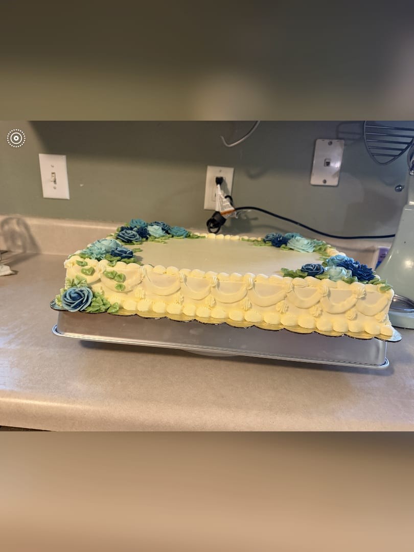 Close view of a sheet cake with blue flowers and a yellow piped border