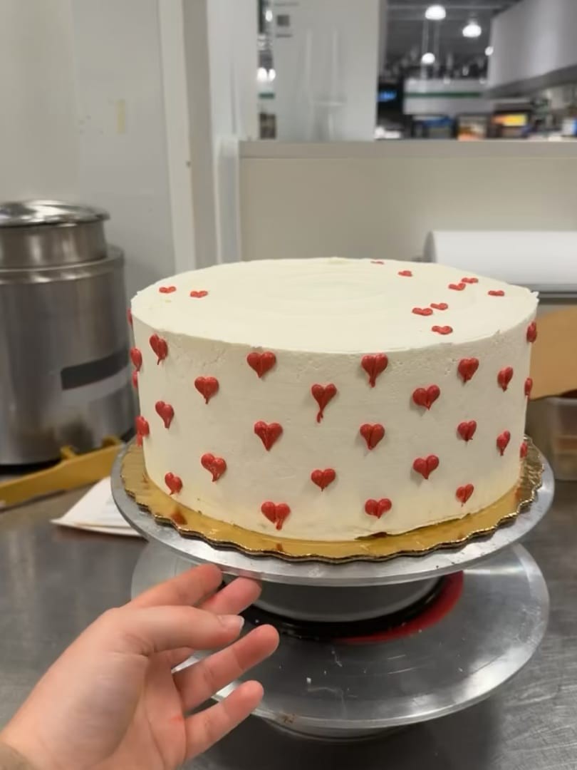 White round cake covered in small red hearts on a turntable