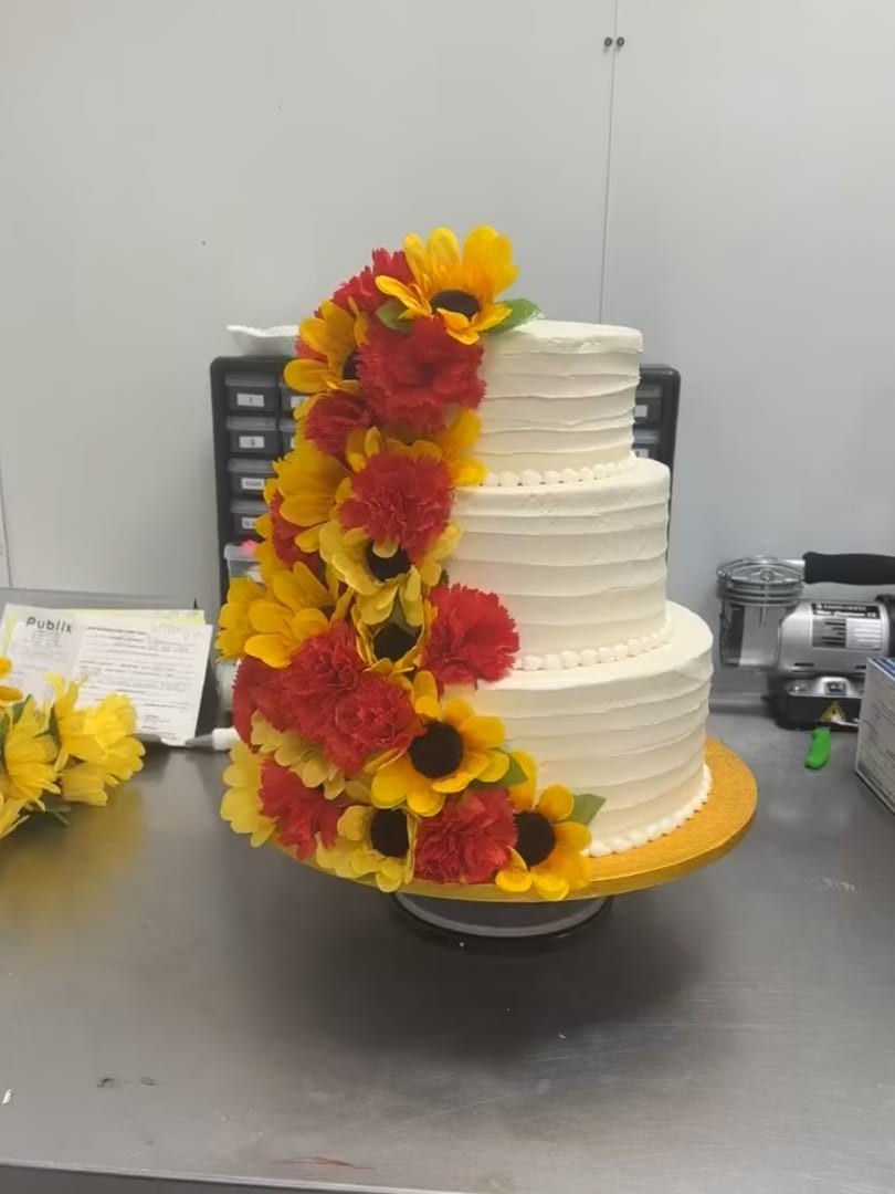 Three-tier white cake with a cascade of red and yellow sunflowers
