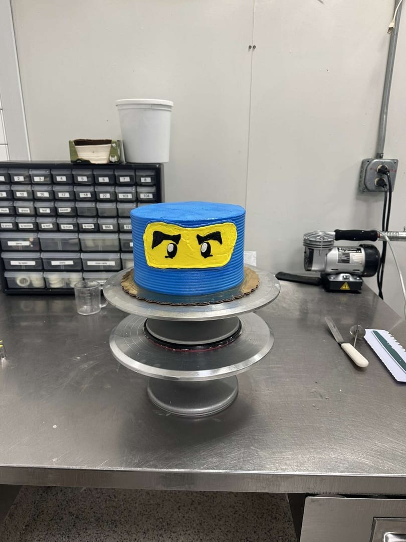 Small blue cake with ninja-style yellow eyes on a cake stand