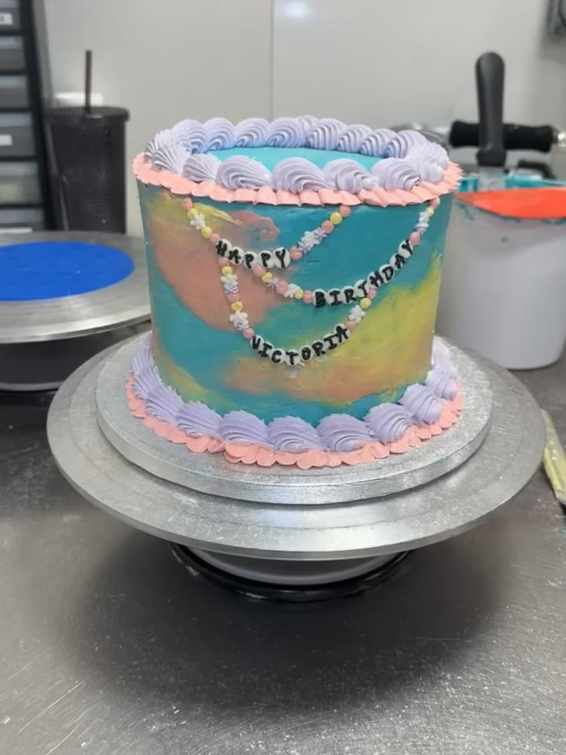 Round cake with blue, pink, and green marbled frosting and pearl-style piping