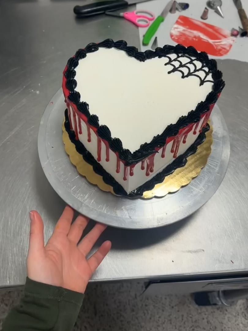 Heart-shaped white cake with black spiderweb piping and red drips