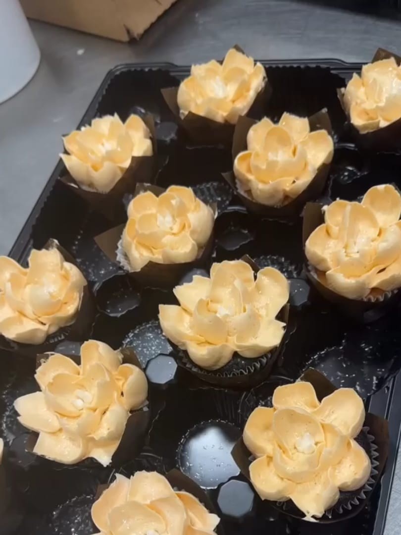 Cupcakes with cream-colored petal-shaped frosting in a black tray