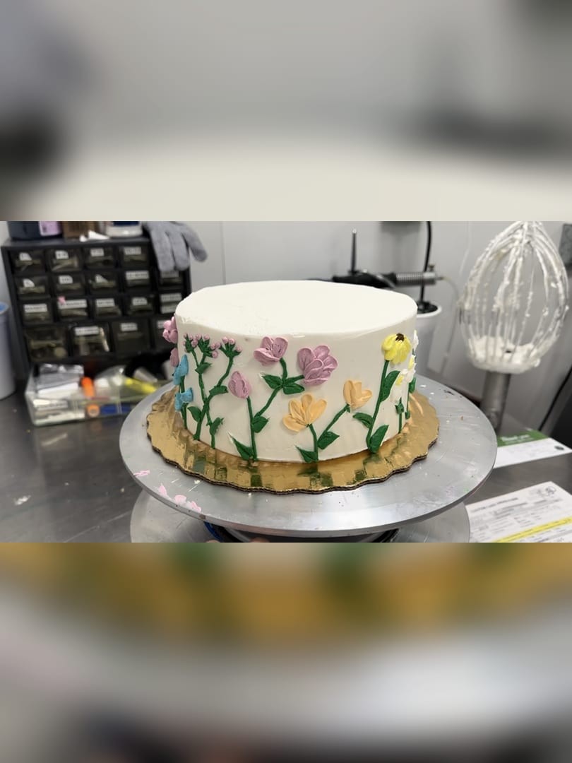 Round white cake with hand-painted flowers on a cake stand
